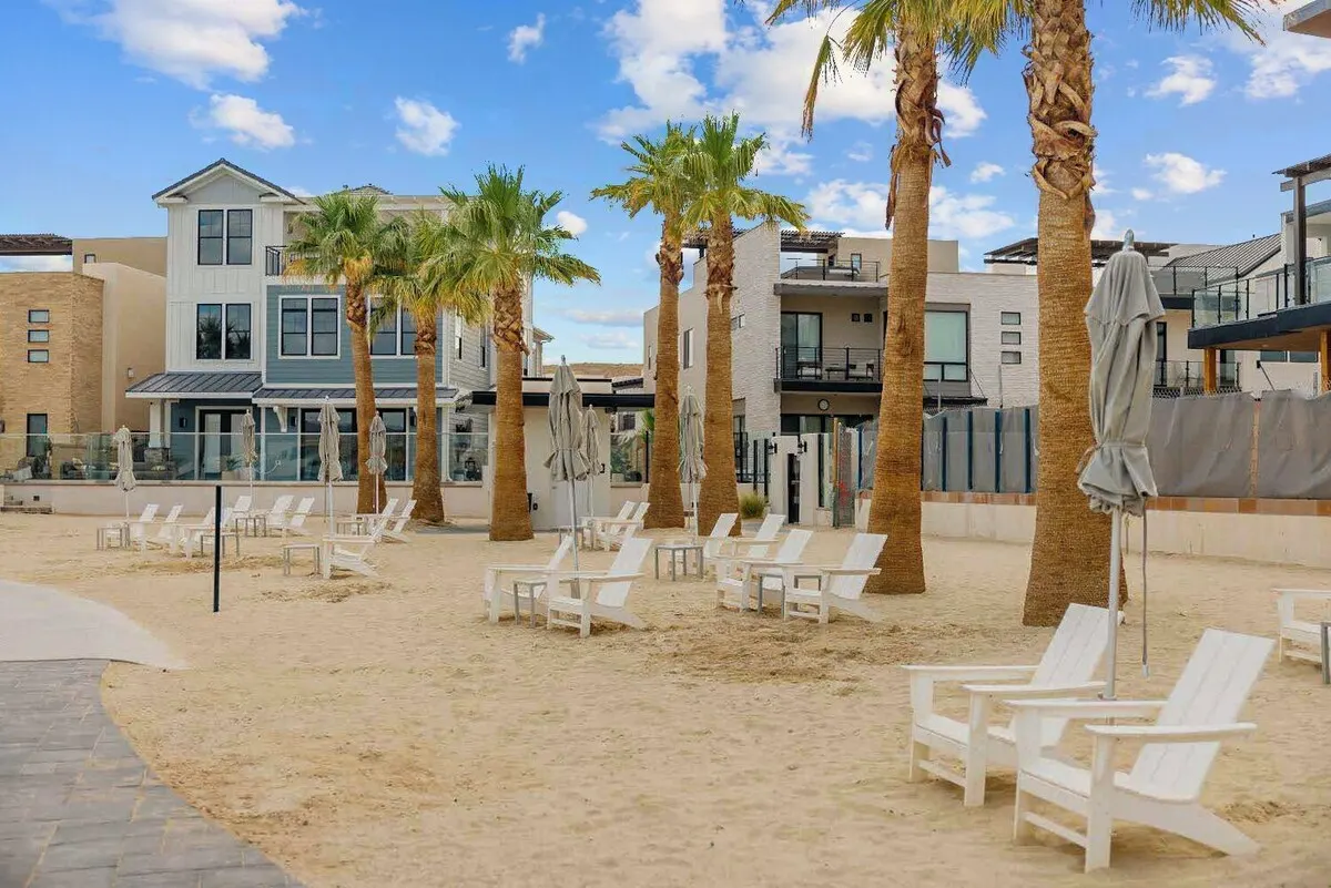 White Adirondack chairs on the sand beach beneath palm trees